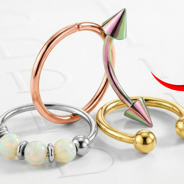 Close up of smiley piercing ring on a plain surface. There is hoop piercing, curverd barbell and horseshoe piercing in here 