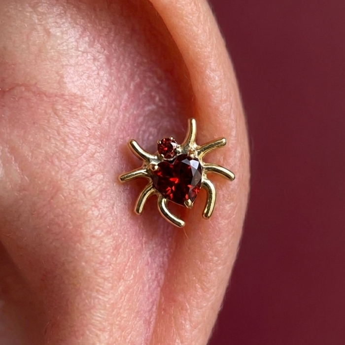 Gold spider heart CZ stud worn in ear cartilage, showcasing flat back fit and sparkling red cubic zirconia stones.