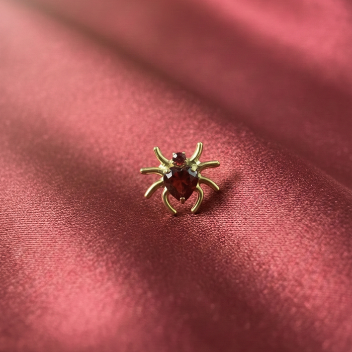Gold spider heart CZ stud displayed on red satin, highlighting its elegant design and titanium build for body jewelry lovers.